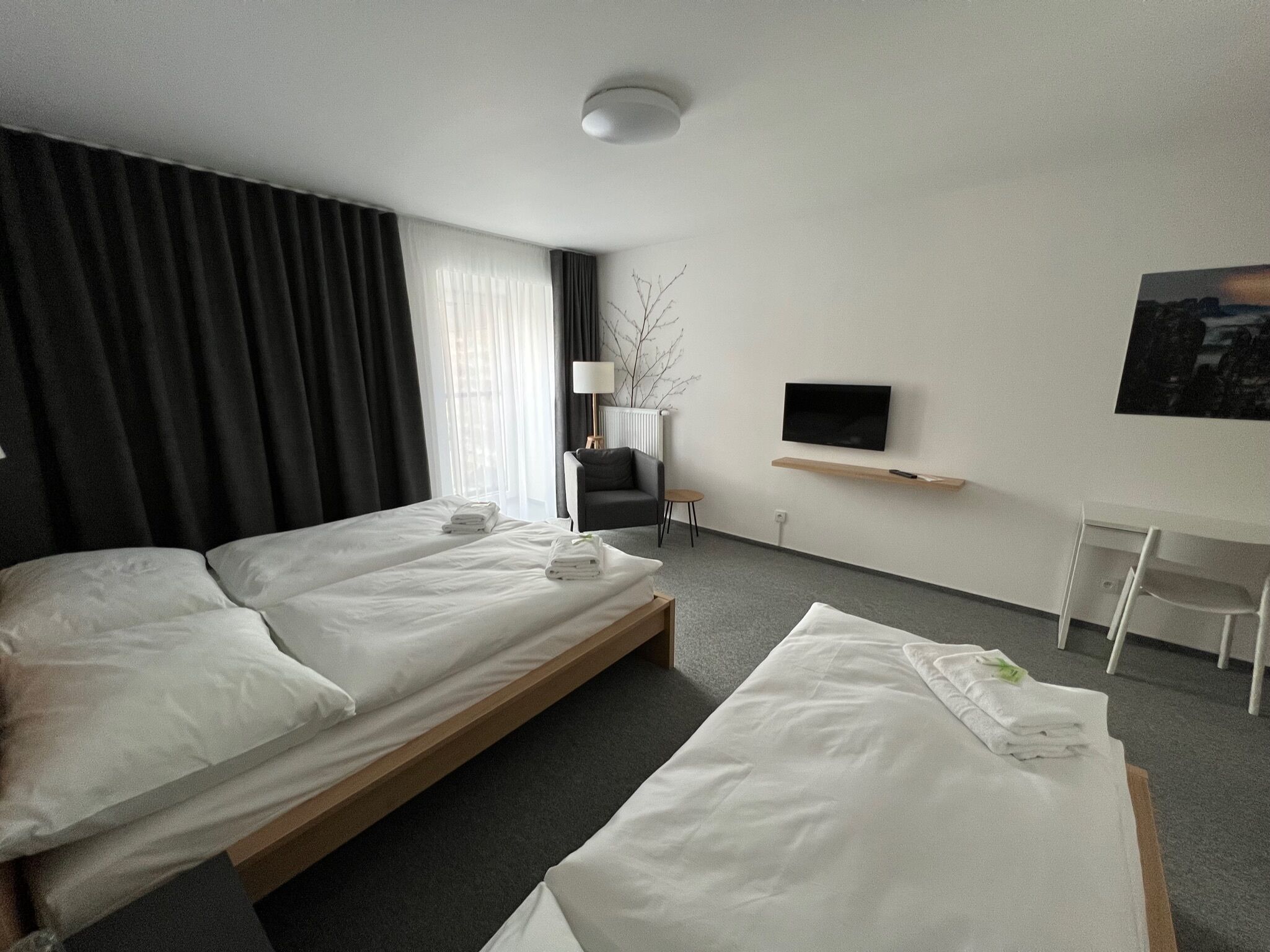 Habitación de hotel con dos camas, un escritorio, una silla, un televisor y una ventana con cortinas.