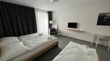 Habitación de hotel con dos camas, un escritorio, una silla, un televisor y una ventana con cortinas.