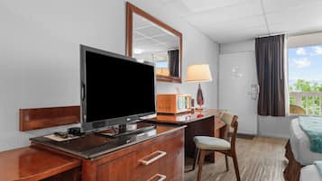 Habitación de hotel con televisor de pantalla plana, cómoda de madera, lámpara, una silla y una cama con vistas al exterior.