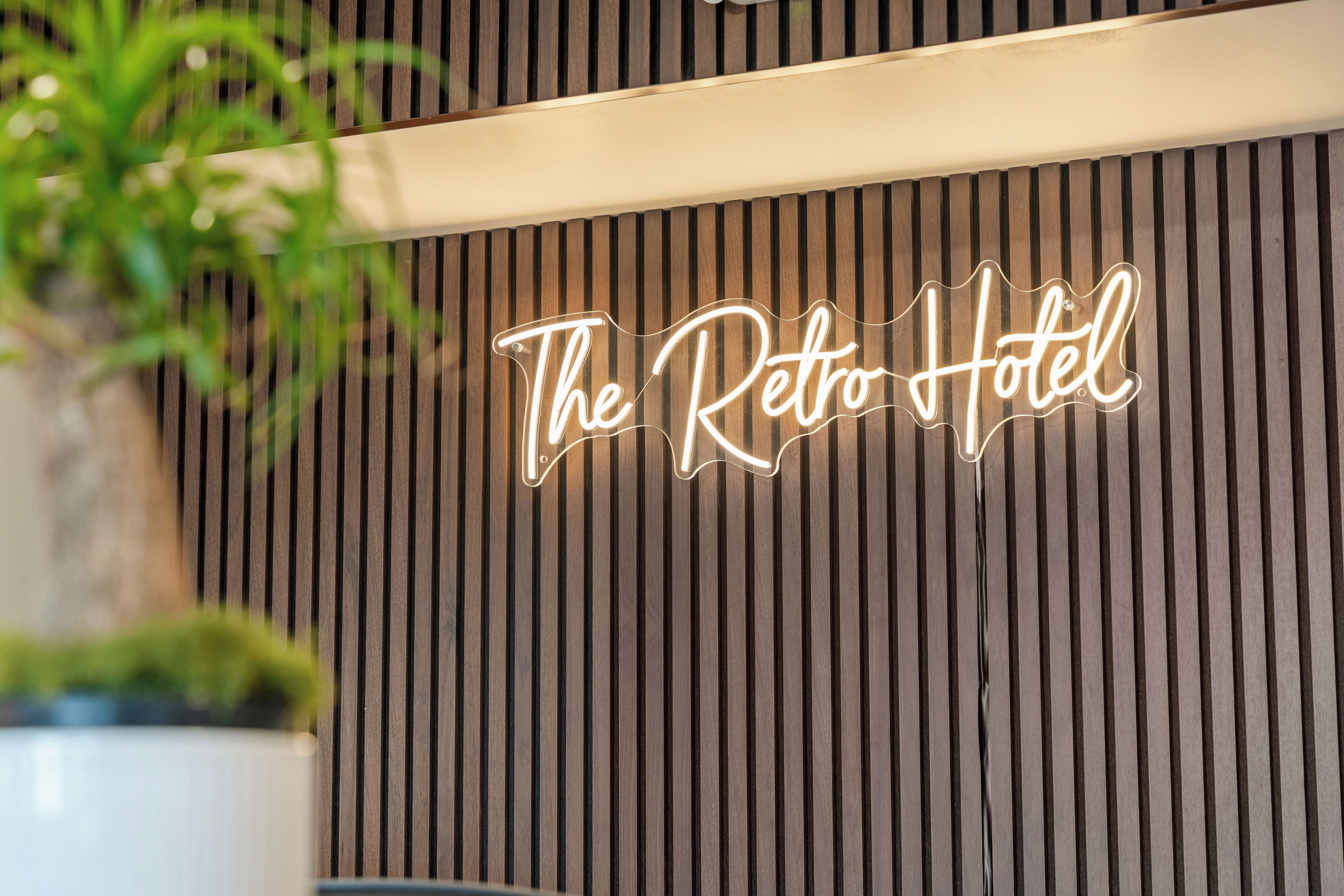 A neon sign with the text 'The Retro Hotel' against a wooden slat wall.