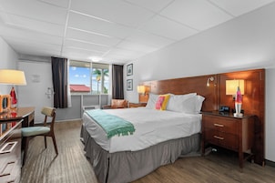 A hotel room with a bed, bedside table, lamp, chair, desk, and a window with curtains.