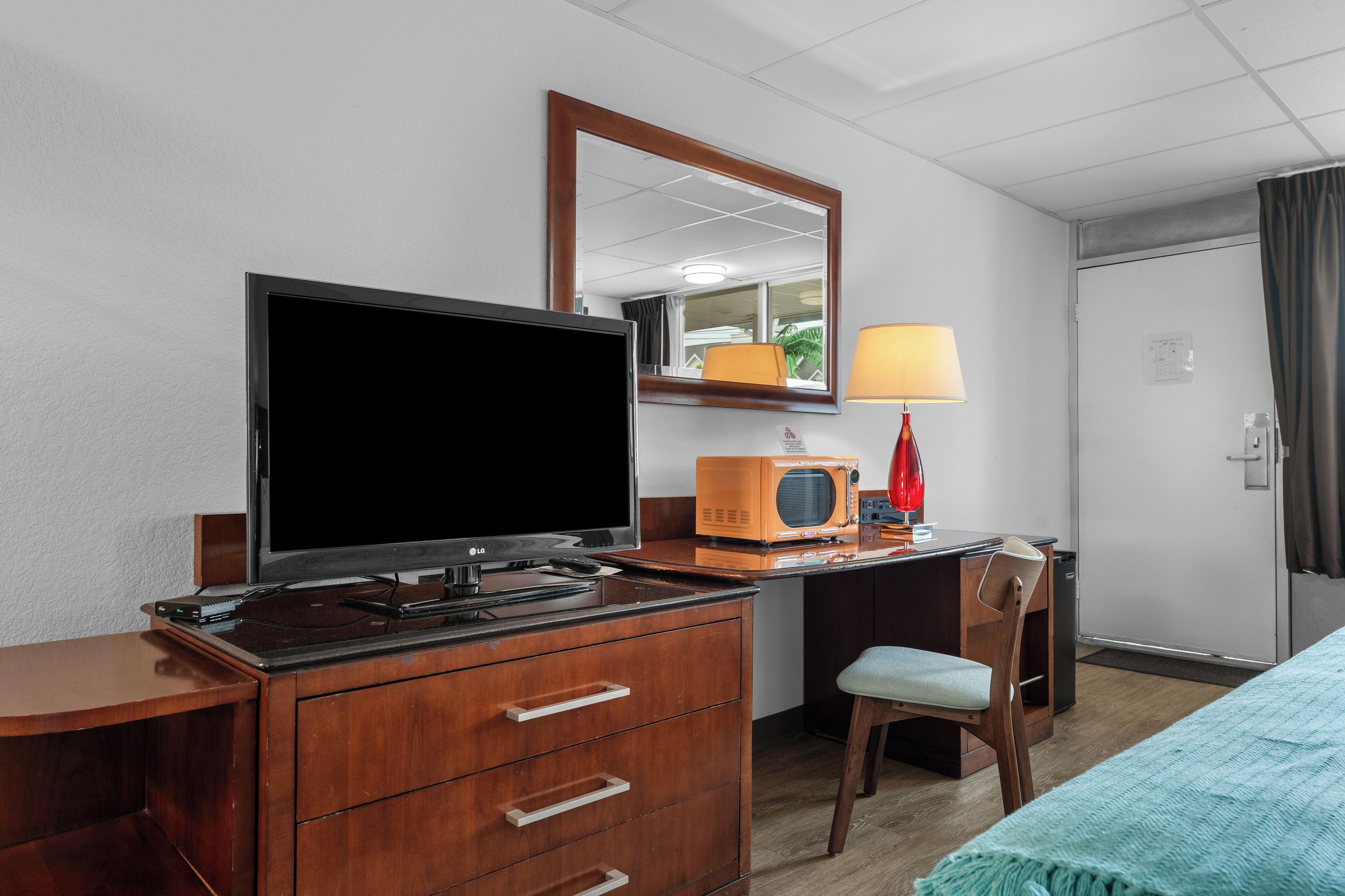 Een hotelkamer met een televisie, een radio, een bureau met lades, een stoel en een bed.