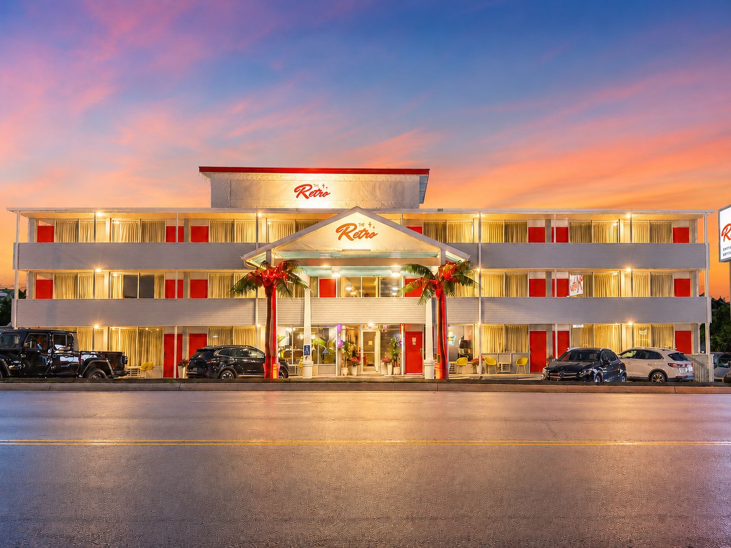 A multi-story hotel with a retro design, featuring a prominent entrance with a canopy and palm trees.