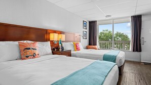 A hotel room with two beds, a wooden headboard, a nightstand with a lamp, and a balcony with a view of trees. - The Retro Hotel (Branson)