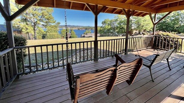 Una terraza techada con bancos de madera y una hamaca, con vista a un lago y árboles.