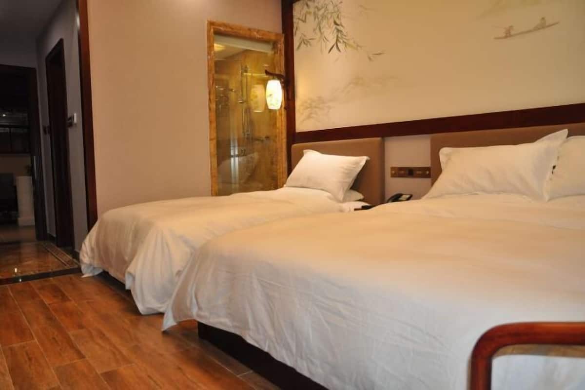 Una camera d'albergo con due letti, pavimento in legno, un grande specchio e un quadro appeso al muro.
