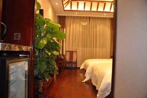 A hotel room with a bed, a chair, a potted plant, and a minibar. - Chunqiu Shuyuan Hotel (Feicheng)