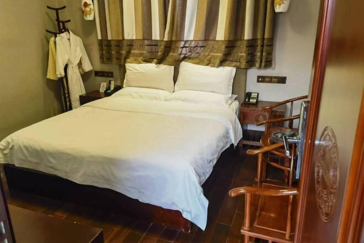 Una camera d'albergo con un letto grande, una sedia di legno, un comodino e un telefono fissato al muro.