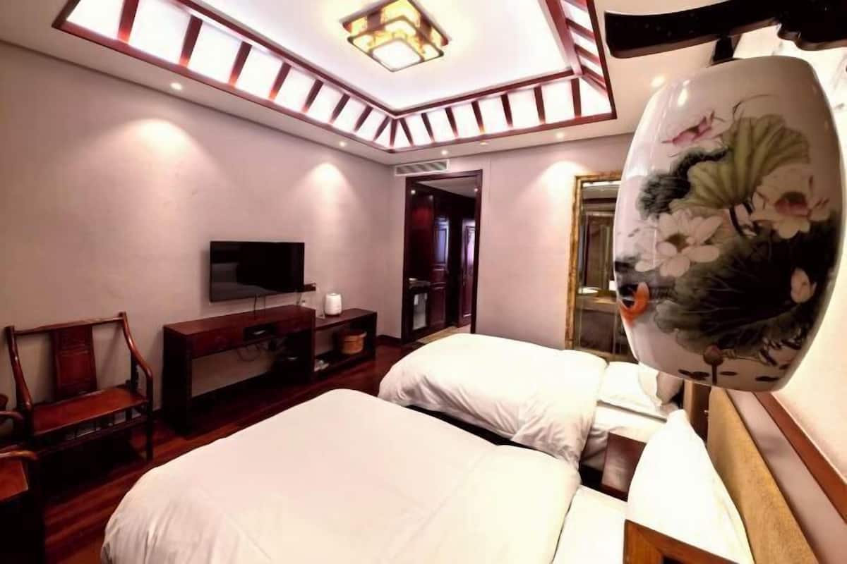 Una camera d'albergo con due letti, una TV a schermo piatto, una panca di legno e un vaso decorativo.