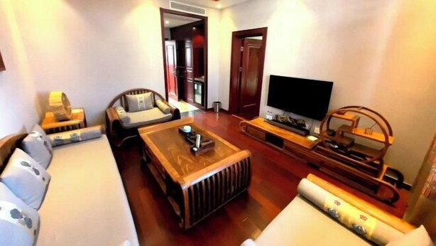 A living room with a sofa, a coffee table, a TV, and a wooden entertainment unit. - Chunqiu Shuyuan Hotel (Feicheng)