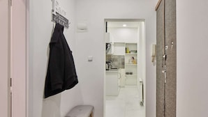 A narrow hallway leading to a kitchen with white cabinets, a bench, and a towel hanging on the wall.