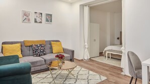 A modern living room with a grey sofa, yellow cushions, a green armchair, and a round coffee table with a vase of flowers.