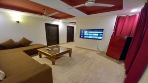 Uma sala de estar com sofá, mesa de centro, TV fixada na parede e ventilador de teto.