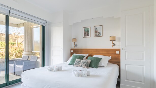 Ein Hotelzimmer mit einem großen Bett, zwei Wandleuchten und Blick durch eine Schiebeglastür.