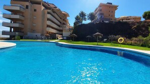 A swimming pool surrounded by a landscaped area with a multi-story building in the background. - Sea Breeze Apartment | Spacious Terrace (Fuengirola)