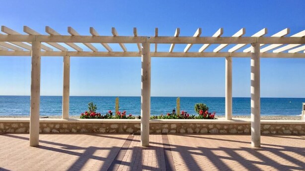 A covered outdoor area with a view of the sea, featuring a pergola structure and a paved walkway. - Sea Breeze Apartment | Spacious Terrace (Fuengirola)