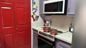 Una cocina con puertas dobles rojas, un microondas blanco, una estufa a gas con ollas y una cafetera.