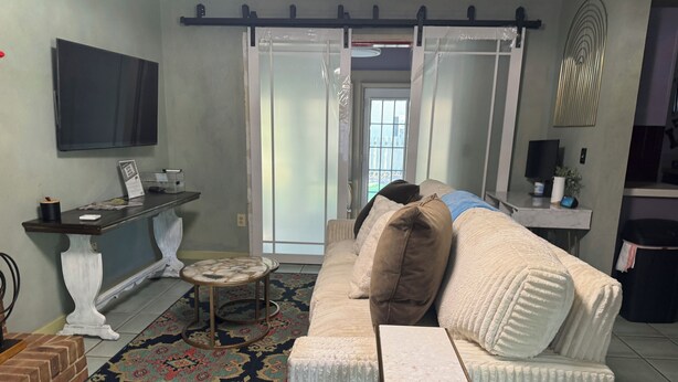 Una sala de estar con un sofá, una mesa de centro, un televisor montado en la pared y un ventanal corredizo que da a un balcón.