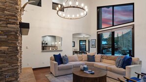 A modern living room with a stone accent wall, a large window with a view, a chandelier, and a sectional sofa. - Spacious East Vail Getaway by Vail Butler (Vail)