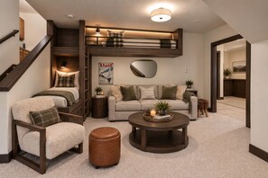 A cozy living room with a sofa, armchair, coffee table, and a staircase leading to a loft.