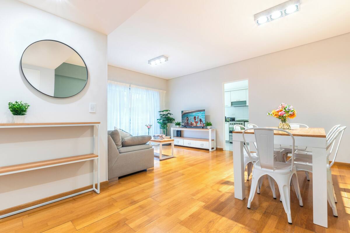 Una sala de estar moderna con sofá, mesa de comedor, sillas y televisor.