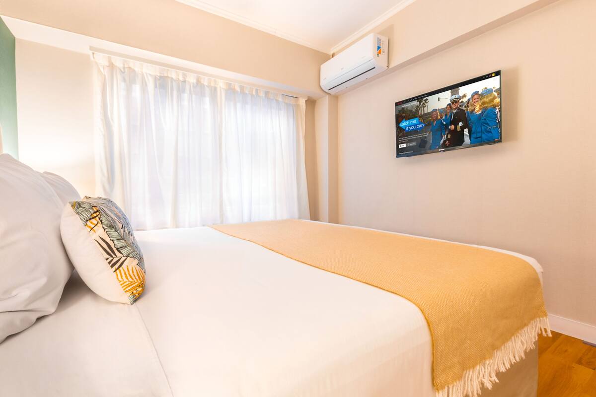 Una habitación de hotel con una cama, un televisor montado en la pared y un equipo de aire acondicionado.