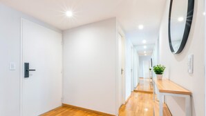 Un pasillo con piso de madera, paredes blancas y un espejo a la derecha.