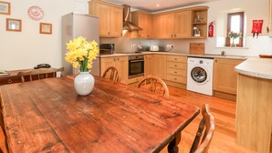 Una cocina compacta con armarios de madera, horno empotrado, lavadora y comedor con mesa y sillas de madera.