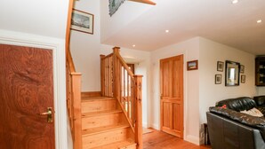 Una escalera de madera que lleva al segundo piso, un sofá de cuero negro y una puerta de madera.
