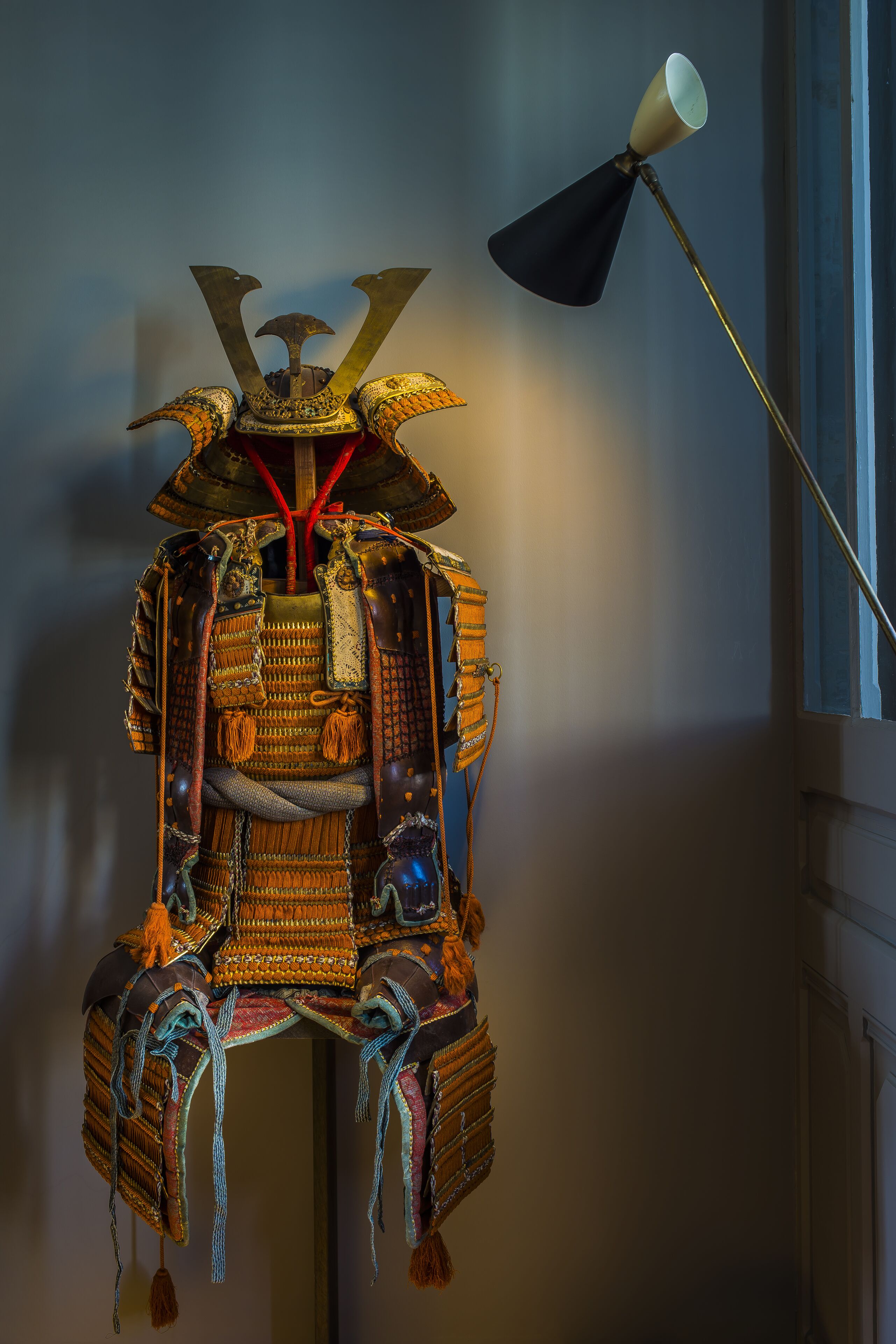 A traditional samurai armor display with intricate designs and a lamp in the background.