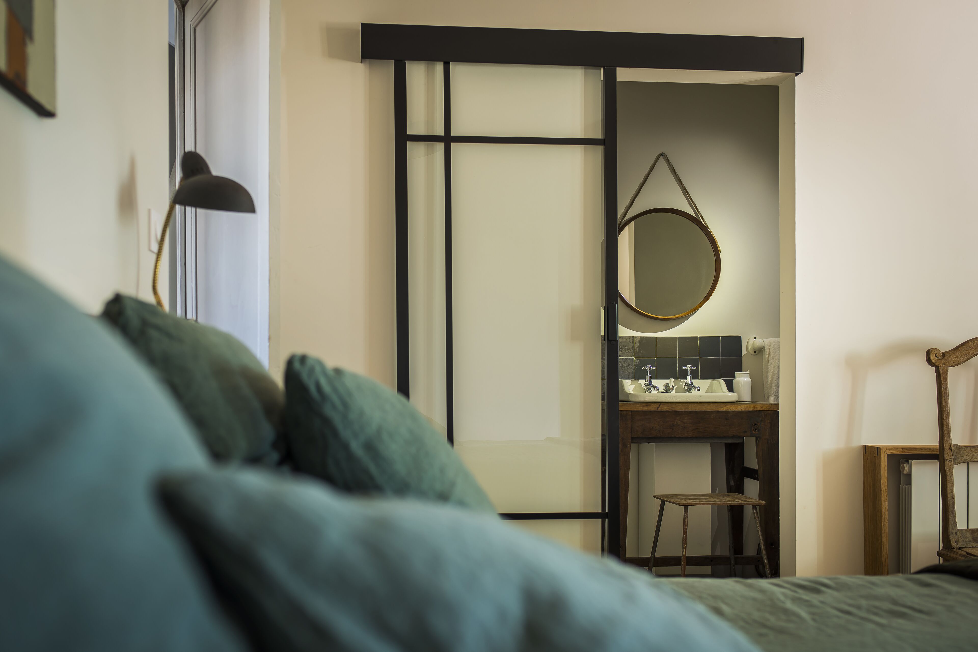 A bedroom with a bed, a bedside table, a mirror, and a small stool.