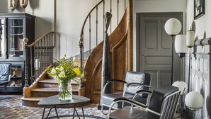 A staircase with wooden steps and a metal railing, a round table with a vase of flowers, and two leather chairs. - LE LANTERNON (Saint-Martin-de-Re)