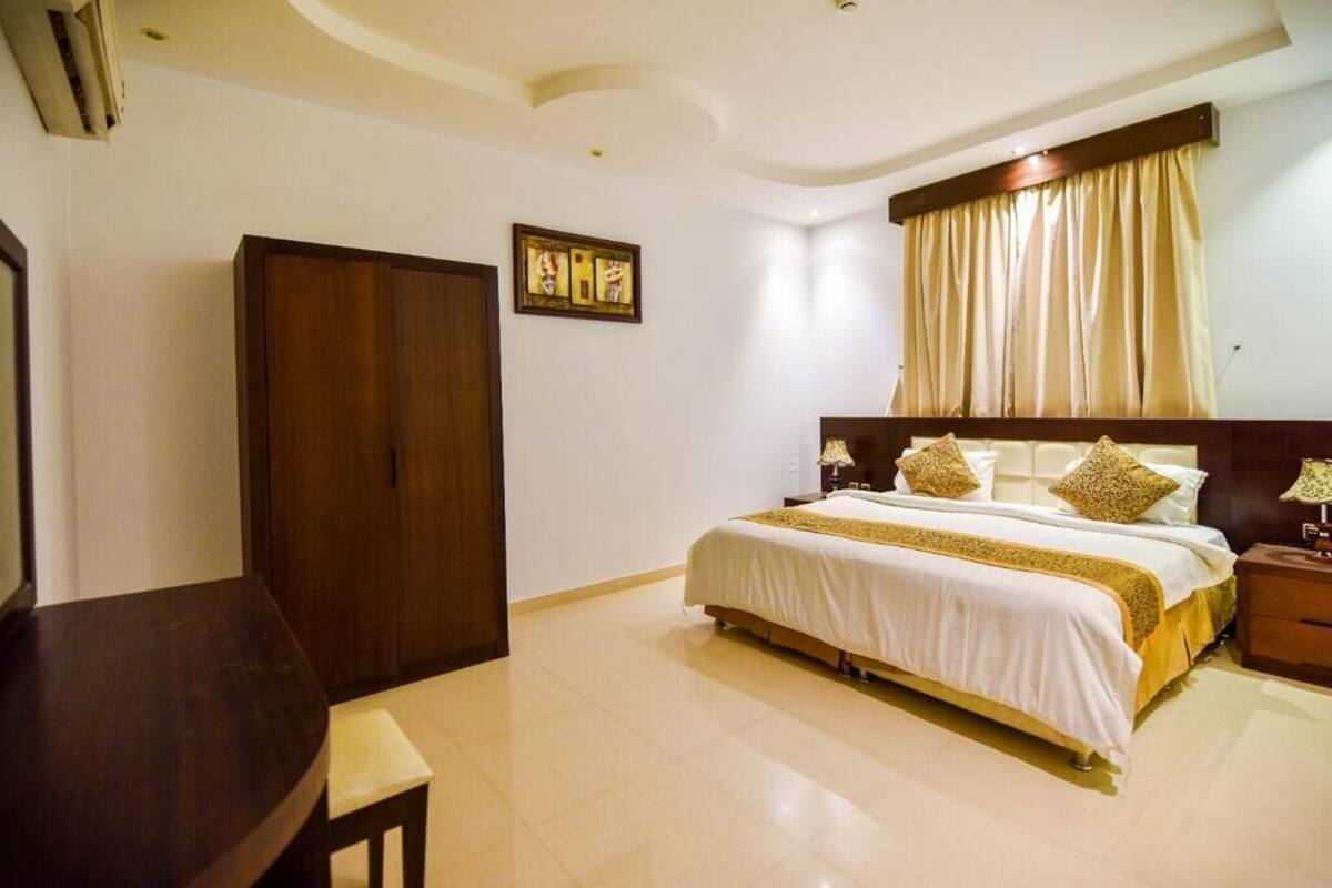 A hotel room with a bed, bedside tables, a desk, and a wardrobe.