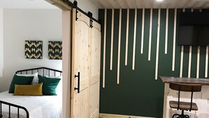 Une pièce comprenant un lit, un bureau avec un tabouret, un téléviseur fixé au mur et une porte coulissante.