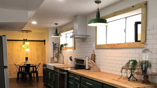 Une cuisine moderne avec des meubles de couleur vert foncé, des plans de travail en bois et des luminaires suspendus.