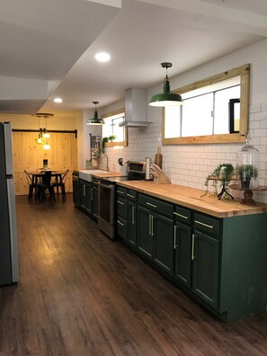 Een moderne keuken met donkergroene kastjes, houten aanrecht en hanglampen.