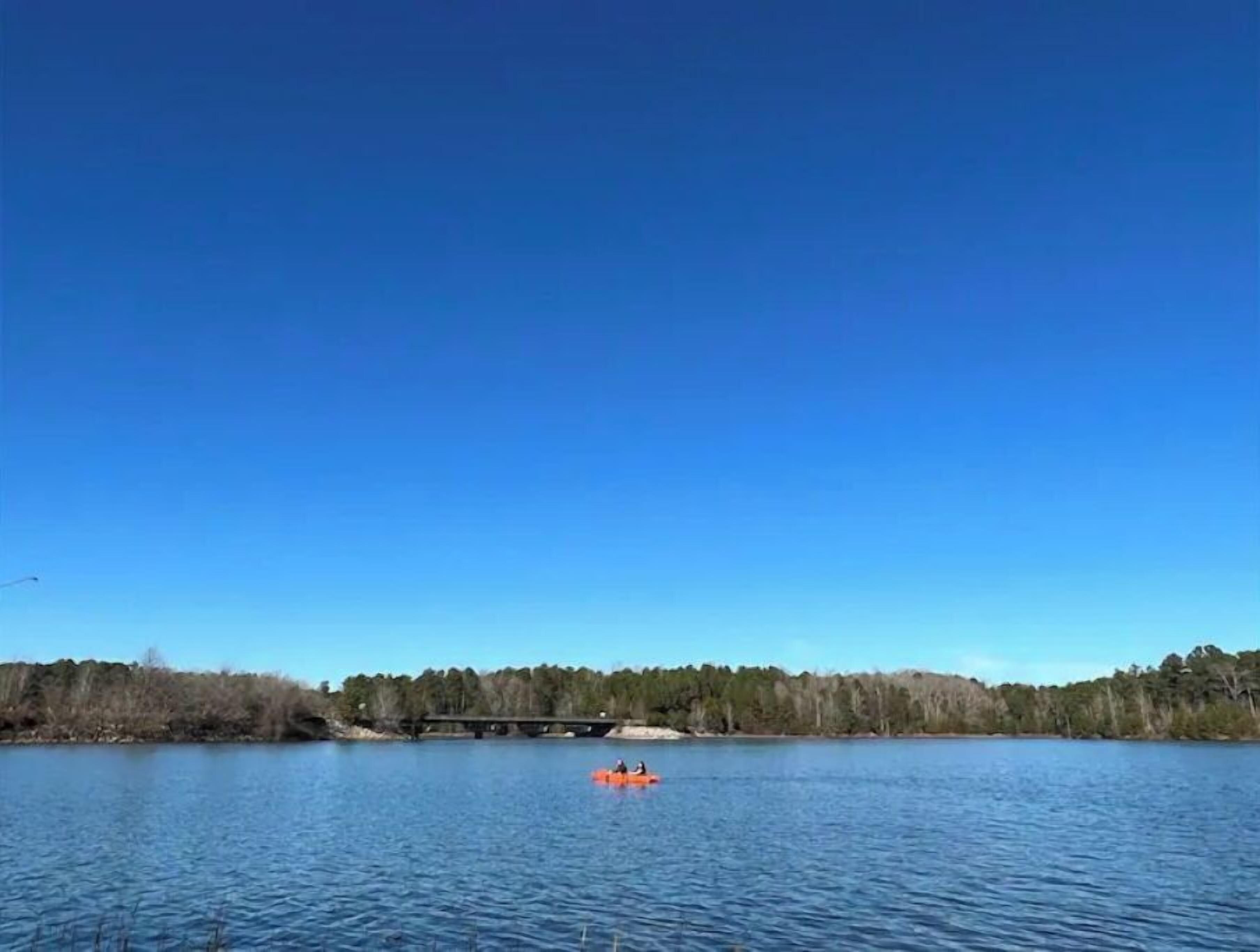 Ein ruhiger See mit blauem Himmel, einer Brücke in der Ferne und einer Person in einem Kanu.