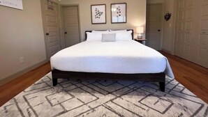 A bedroom with a large bed, two framed pictures on the wall, a ceiling fan, and a rug.