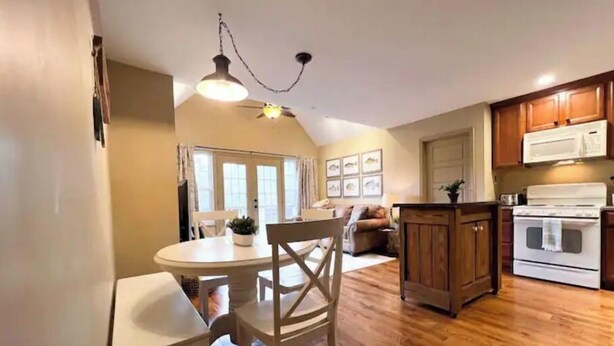 A compact kitchen with wooden cabinets, a white stove, and a dining area with a round table and chairs.