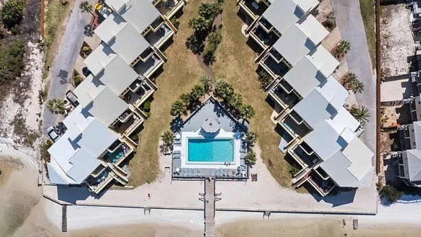 Luftaufnahme eines Resorts mit einem zentralen Pool, der durch eine Brücke mit mehreren Gästezimmern verbunden ist.