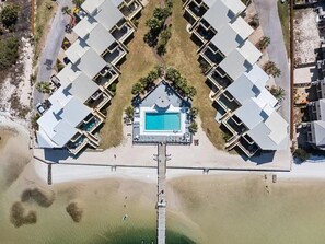 Vue aérienne d’un complexe hôtelier doté d’une piscine centrale, reliée à plusieurs chambres par un pont.