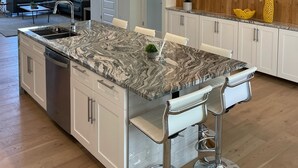 A modern kitchen with a marble island, white cabinetry, and stainless steel appliances.