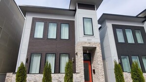 A modern two-story residential building with a stone facade, multiple windows, and a red door.