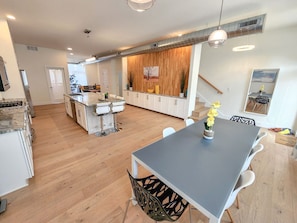A modern kitchen with a central island, white cabinetry, and a dining area with a grey table and white chairs.