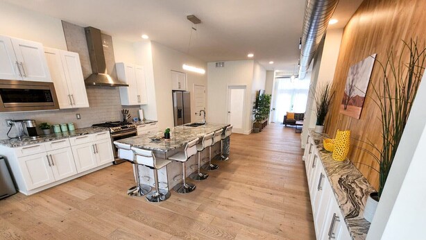 A modern kitchen with white cabinetry, a central island with bar stools, and a wooden floor.