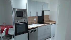 A modern kitchen with stainless steel appliances, a wooden countertop, and white cabinetry. There is a dining area with a red tablecloth and white chairs. - 30 m2 furnished apartment near shops and metro (Sotteville-lès-Rouen)