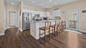 A modern kitchen with white cabinets, stainless steel appliances, and a marble island with bar stools. - Oceanfront Family Retreat / Pool, Hot Tub, Elevator, Well stocked kitchen (North Topsail)