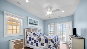 A bedroom with a bed, a ceiling fan, a TV on a dresser, and large windows with curtains. - Oceanfront Family Retreat / Pool, Hot Tub, Elevator, Well stocked kitchen (North Topsail)