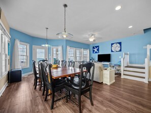 A spacious living area with a dining table, chairs, a TV, and a staircase.