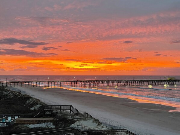 A beach with a wooden boardwalk and a pier extending into the ocean.